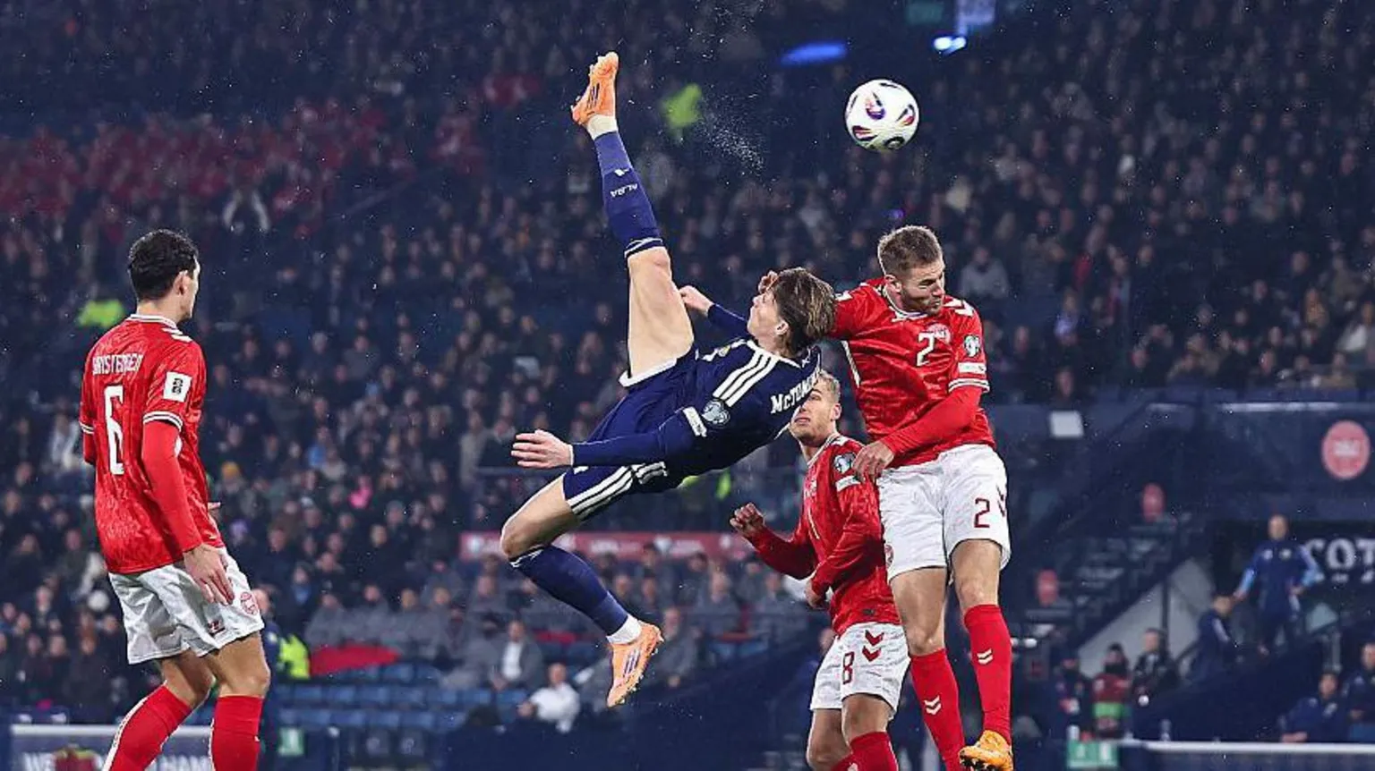  Scotland footballer in a blue strip produces and overhead kick as three Denmark players in red tops and white shorts try to challenge him