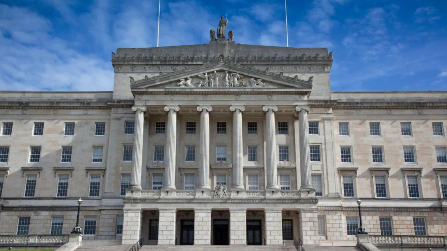  The front of Stormont from the outside. The building is cream stone and has pillars and engravements on it.