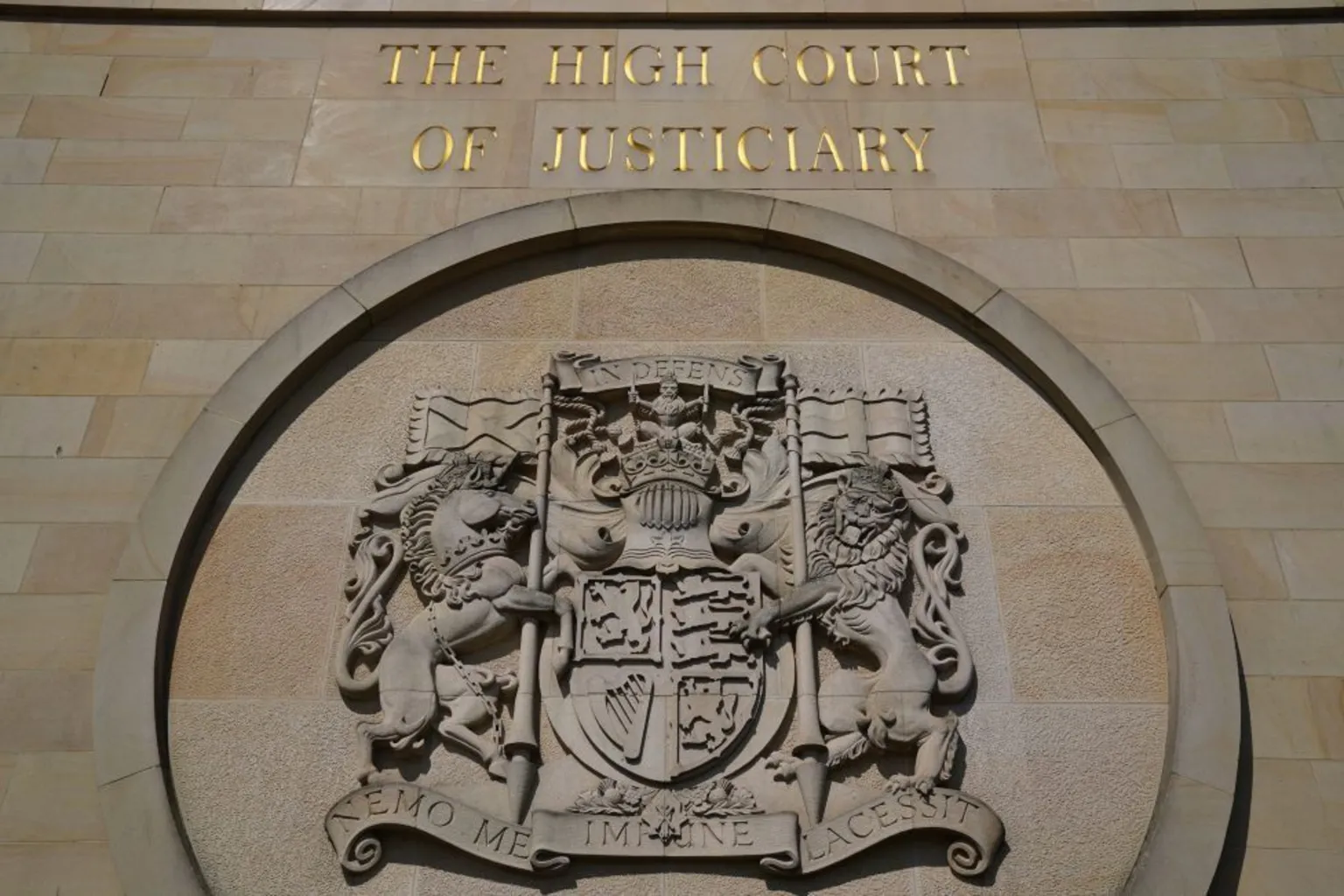  The wall of a sandstone building with a crest. Gold letters above it read 