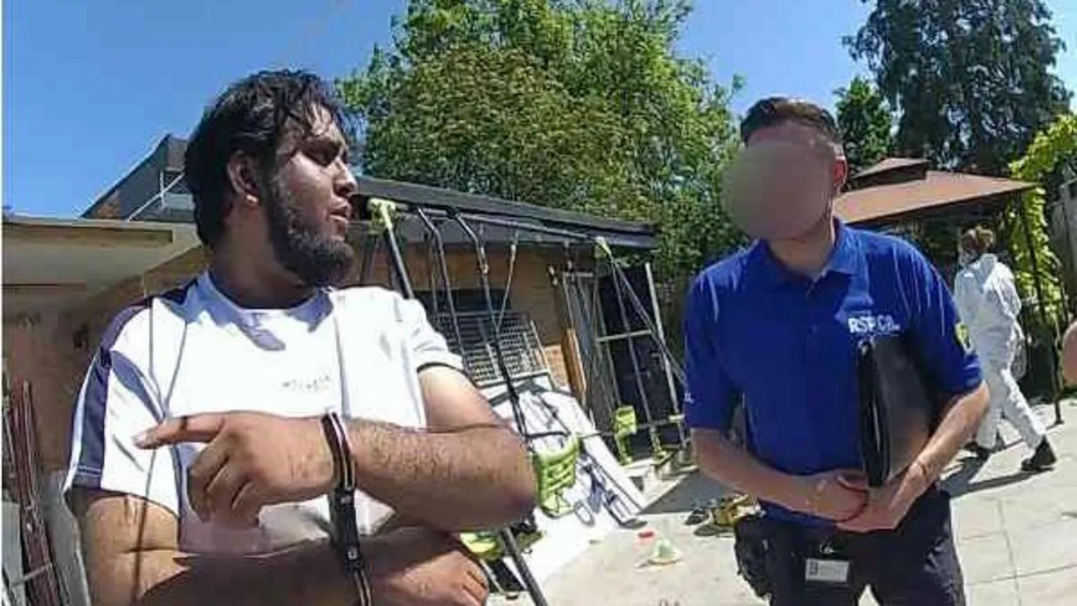 Essex Police A man in handcuffs and a white top. Next to him is a man from the RSPCA with his face blurred, wearing a blue top. They are standing outside. 