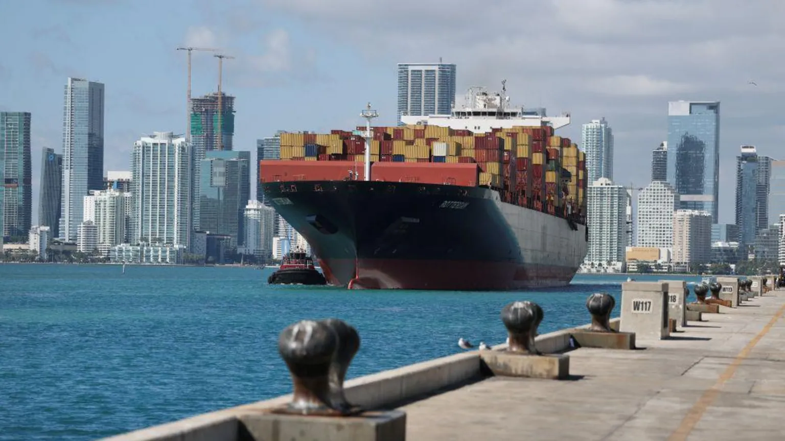  A large container ship with lots of cargo on board is in foreground with Miami skyline behind 