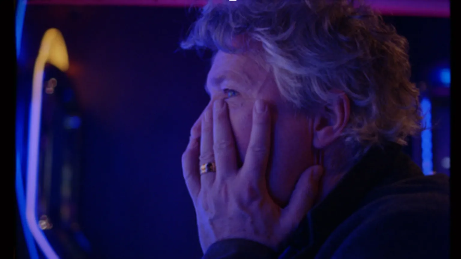 Globe Originals, Stille Productions, Tara Films and Hopefield A screenshot of Aidan Gillen in Nostalgie, with his head in his heads in a dark casino room in a ferry. He has short, wavy grey hair and is wearing a gold ring wedding ring. 