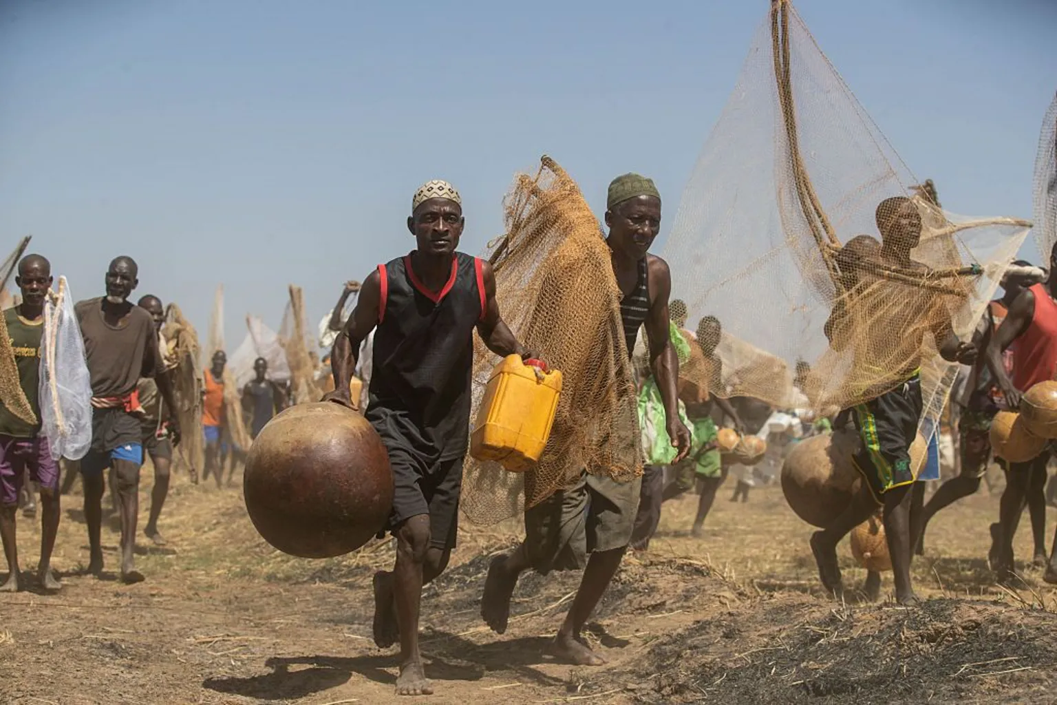 AFP via Fishermen run towards the Matan Fada river. They're holding nets and gourds. One man in the front of the image can be seen holding a yellow jerrycan.