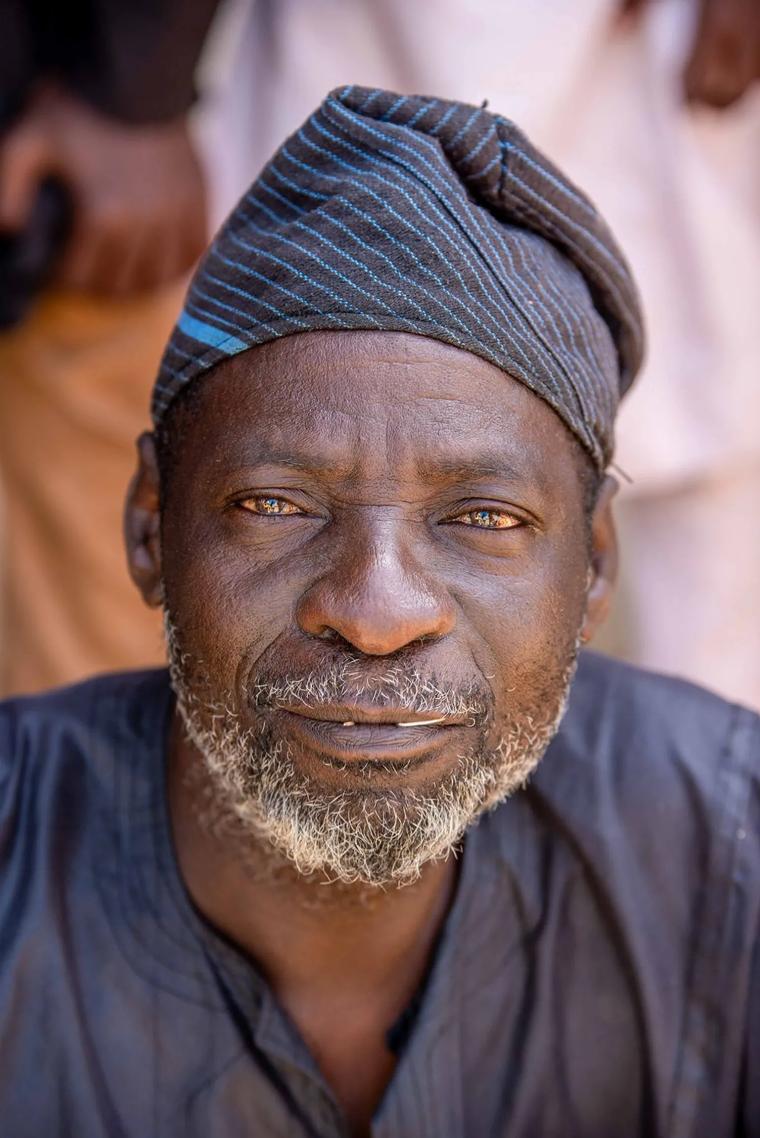 Sani Maikatanga A close-up head-and-shoulders portrait of a man in a dark blue shirt and dark blue cap.
