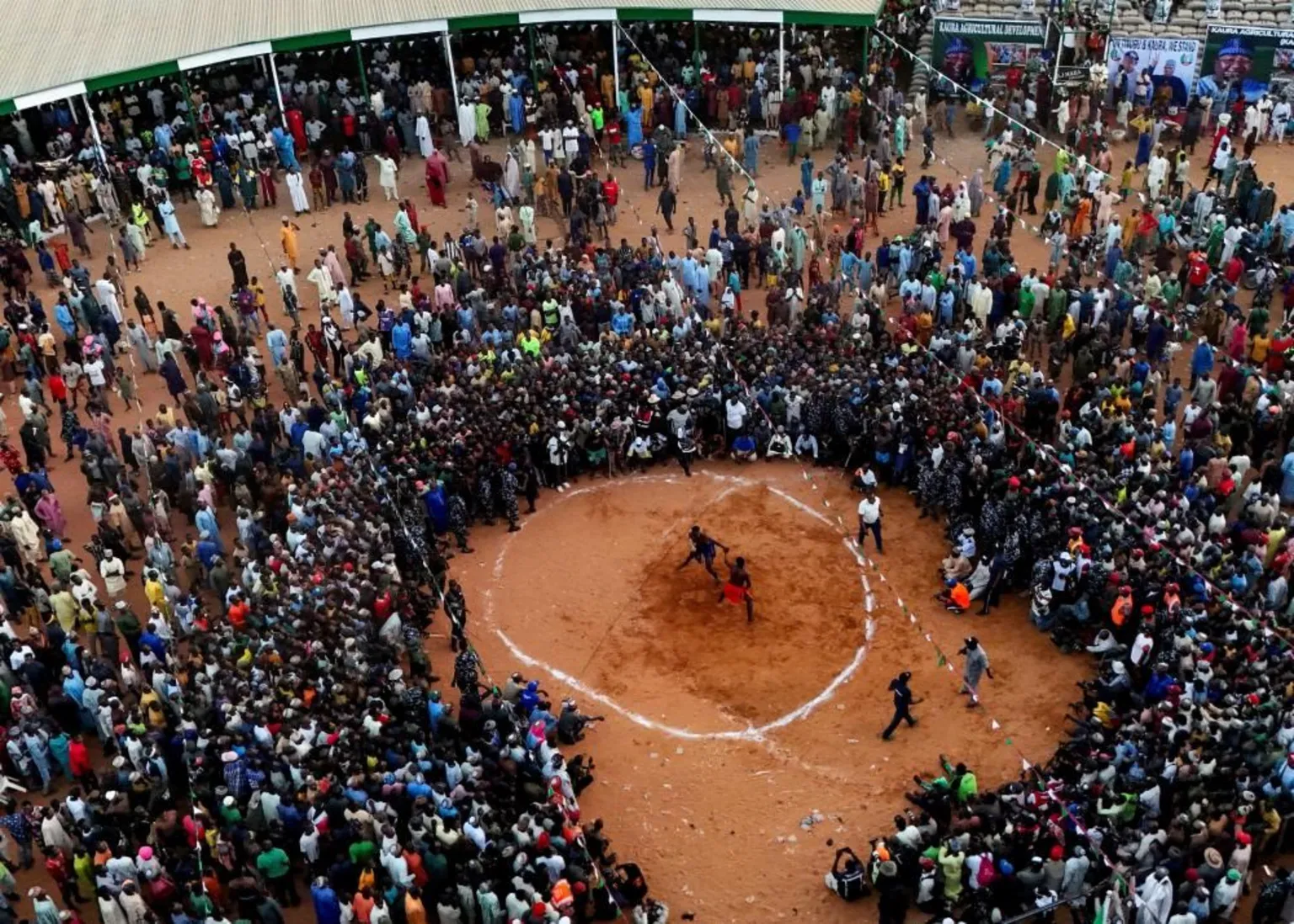  A drone view shows people gathering to watch Dambe fighters compete in the ancient Nigerian combat sport . A white circle drawn on the ground can be seen and the two fighters are inside.
