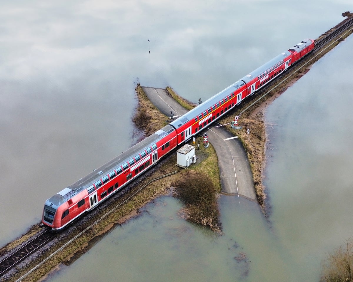 Red train passes over small section of road cut off by flood waters at either end