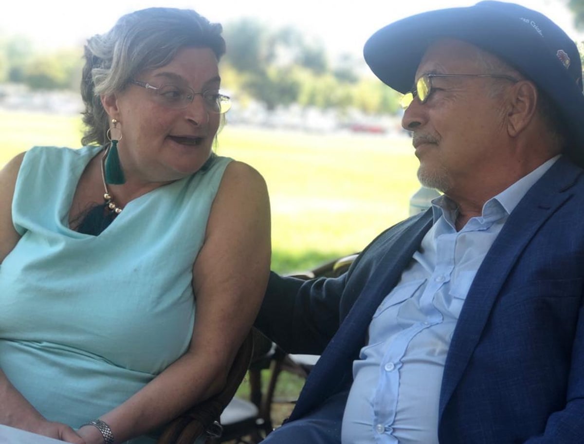 An older couple sit at a table with green space behind them