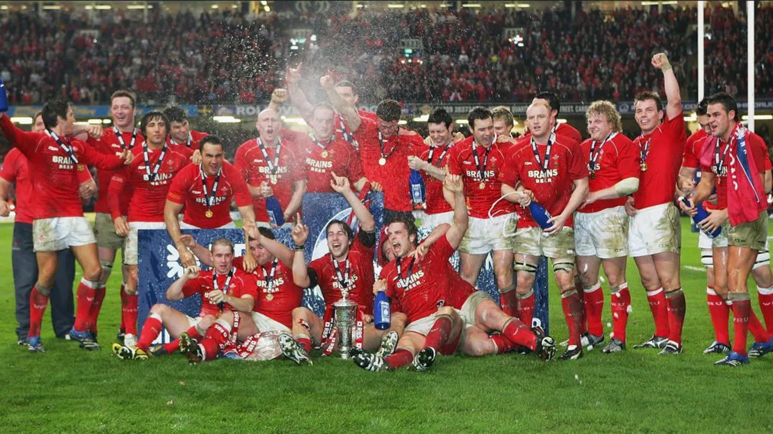  Wales players celebrate on the pitch - they are all in red shirts and white shorts.
