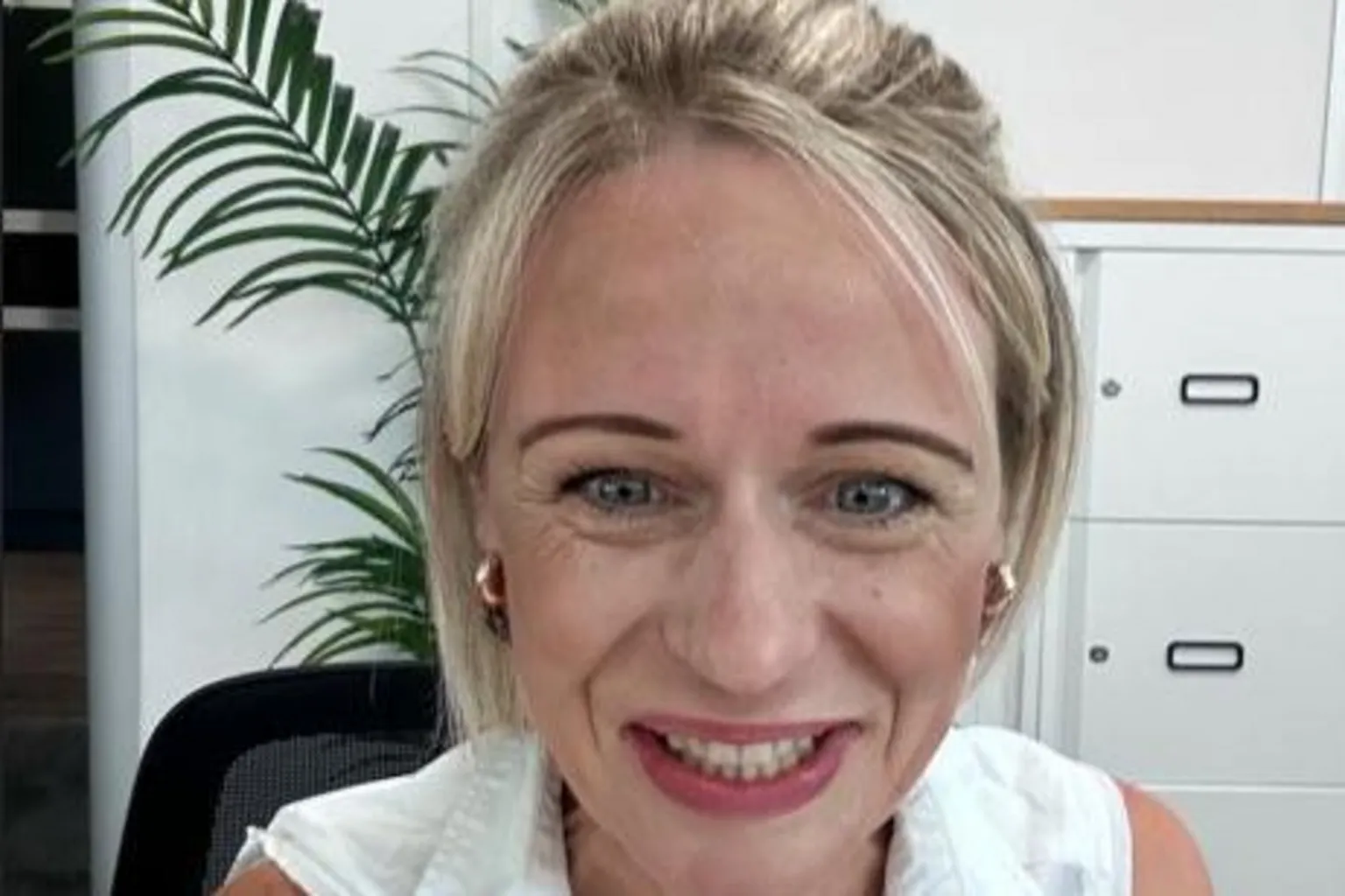 Aisling Pigott Aisling, wearing a white top, smiles at the camera. She has blonde hair and is wearing gold earrings. White filing cabinets and a plant can be seen behind her.