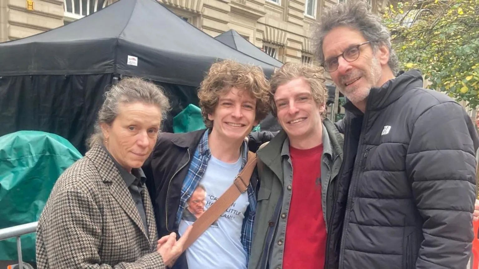 Paul Cowie Two brothers with wavy brown hair smile as they pose for a picture of a middle-aged woman with her hair tied back and wearing a tweed jacket and a man with greying hair and glasses wearing a black jacket