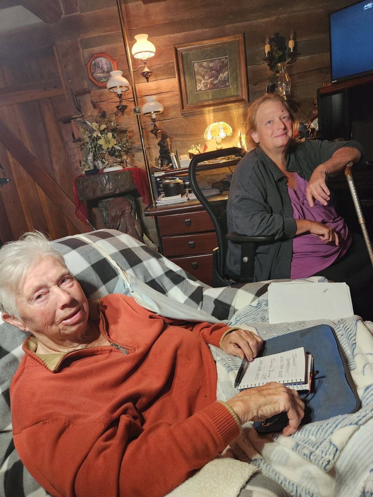 An older woman on a couch, with another woman in a chair behind her