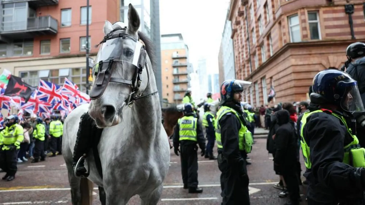 EPA/Shutterstock A police officer is on a police horse which has a protective clear shield over its eyes in a city centre street. Around two other police officers are on horseback behind and multiple police officers are wearing helmets. A crowd of people waving union jack flags can be seen on the left hand side.