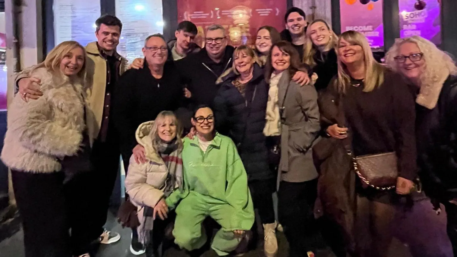 Jade Franks Jade in a green tracksuit is crouching in front of a large group of people. They are all smiling at the camera with their arms around each other. 