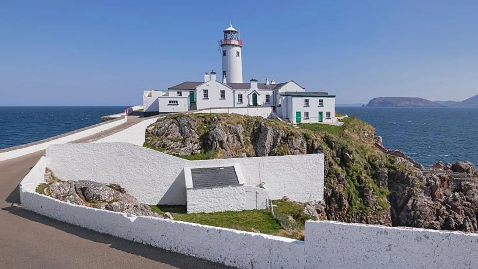 Getty A large white building with a number of doors and windows sits on top of a cliff face. A red and white lighthouse is visible over the structure. A large body of water and rocks are visible in the background