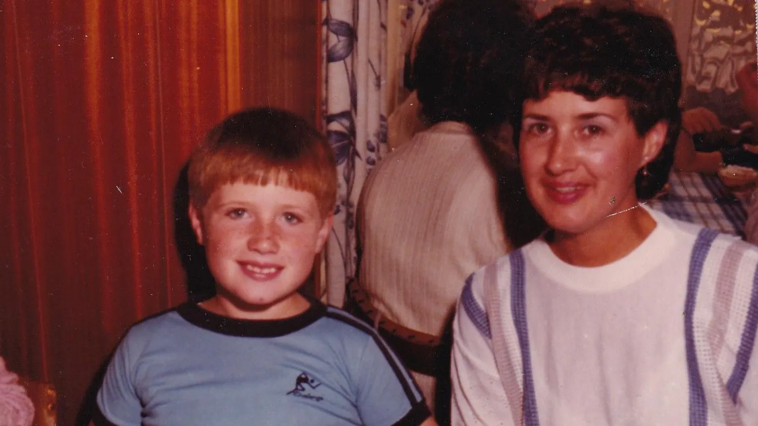 Family photo Photograph of a young Dale Morgan (left) pictured with his mother Judith Rhead(right). Judith has brown short hair and wears a white and purple sweater, while Dale wears a blue and black t-shirt and has short ginger hair and blue eyes. 