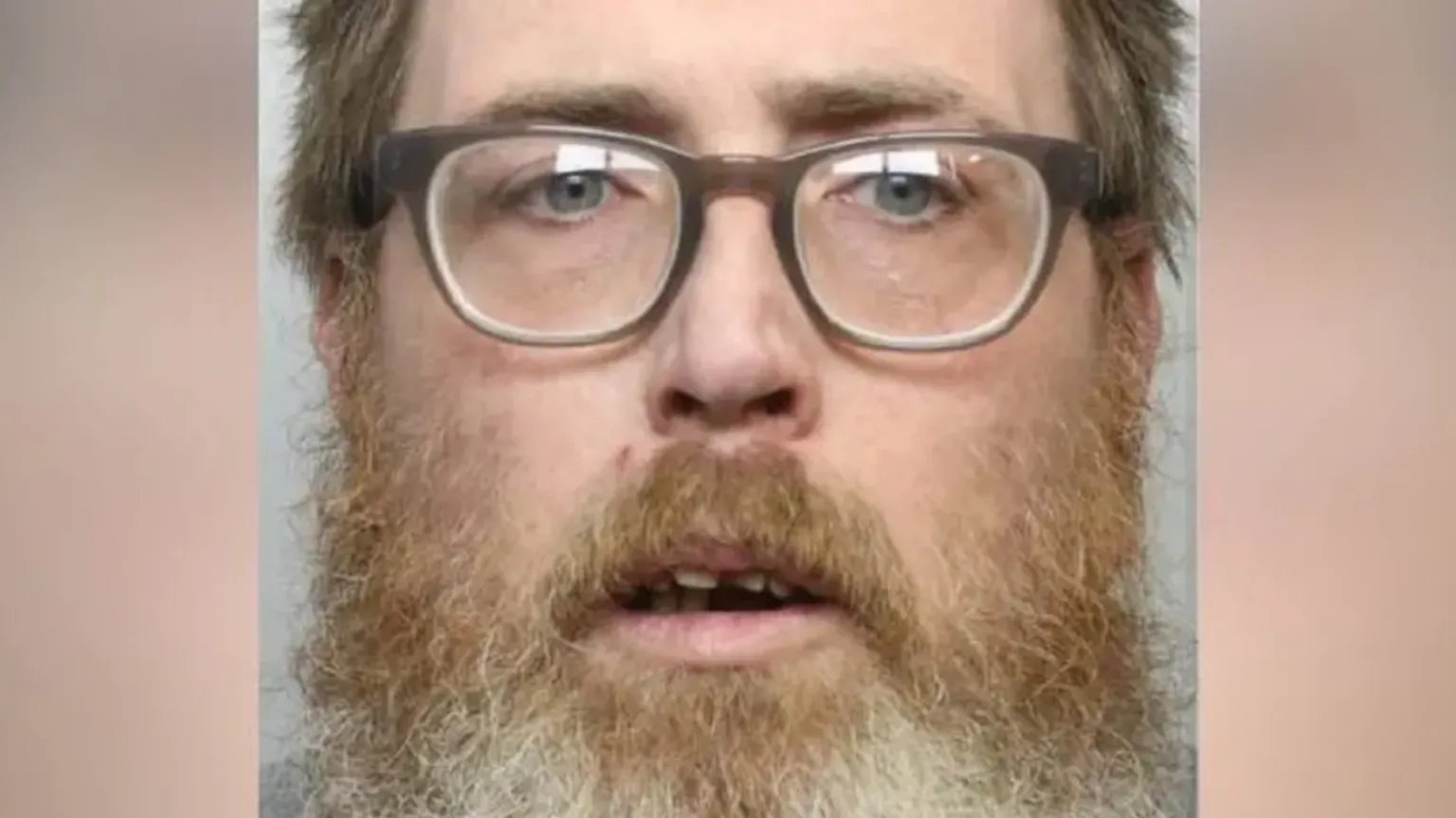 Dyfed- Powys Police Mugshot photograph of Dale Morgan, 42. He has a long shaggy ginger and grey beard, short ash strawberry blonde hair and blue eyes. He wears square rimmed reading glasses and looks confused into the camera, with his mouth part open revealing some of his teeth. 