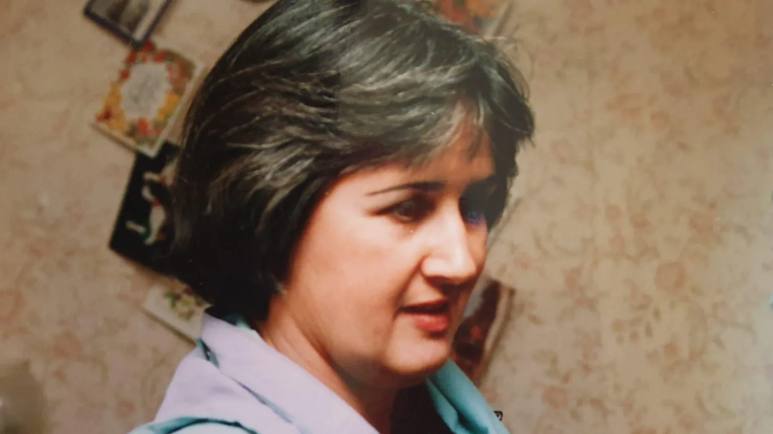 Family photo Archive side profile photograph of Judith Rhead. She has brown short hair, fringed at the front. Behind her a wall covered in cards can be seen. She has brown eyes. 