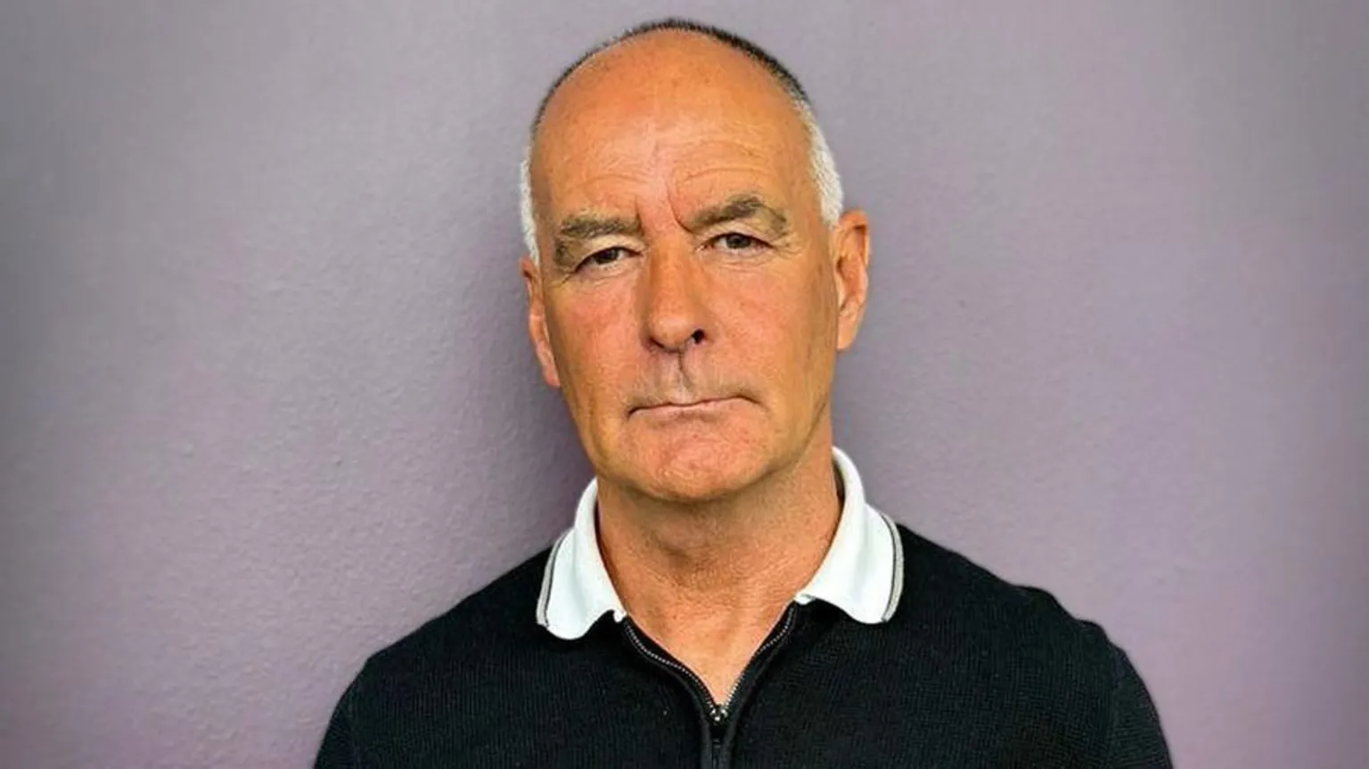 Tommy Sheridan has cropped grey and white hair and wears a black top with a white collar