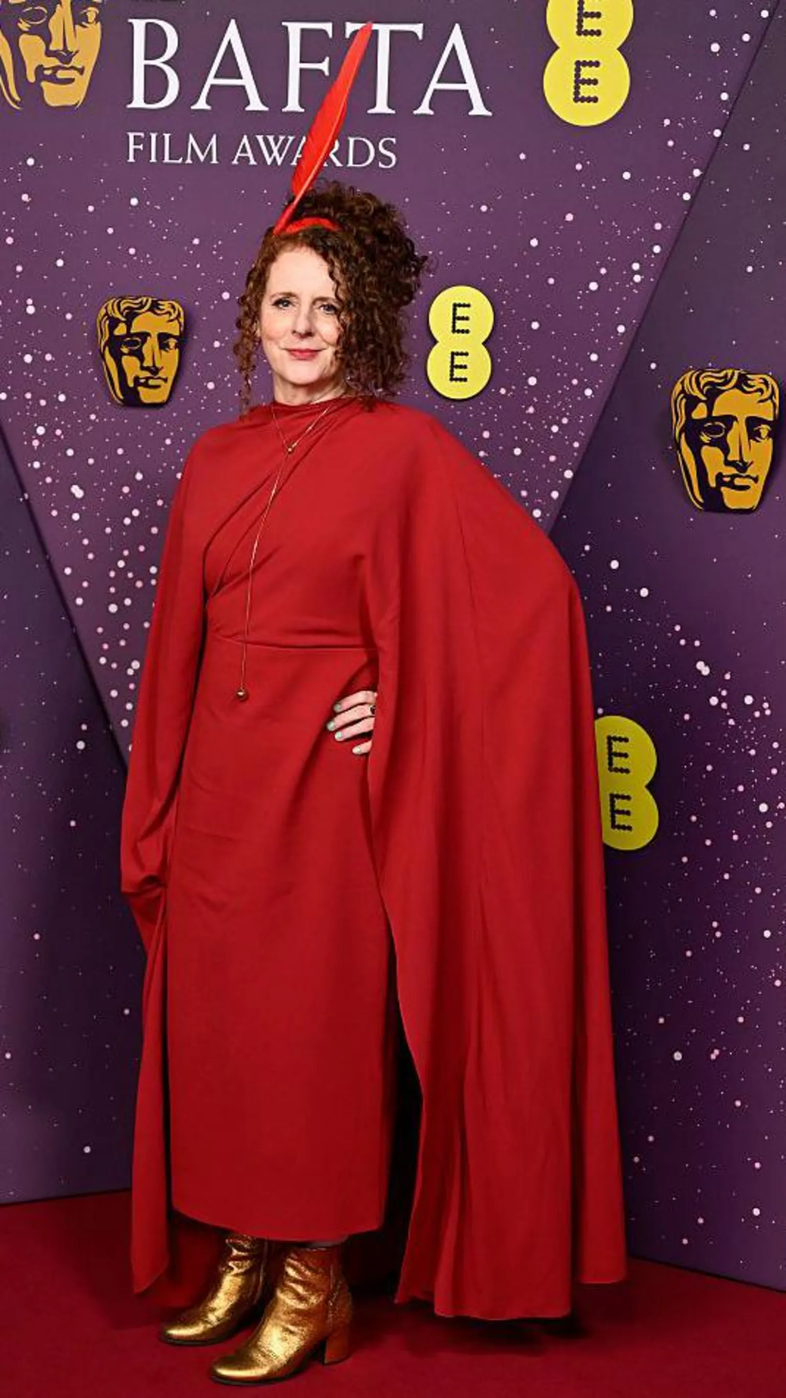  Maggie O'Farrell in a long, red outfit with gold boots and a bold red fascinator 