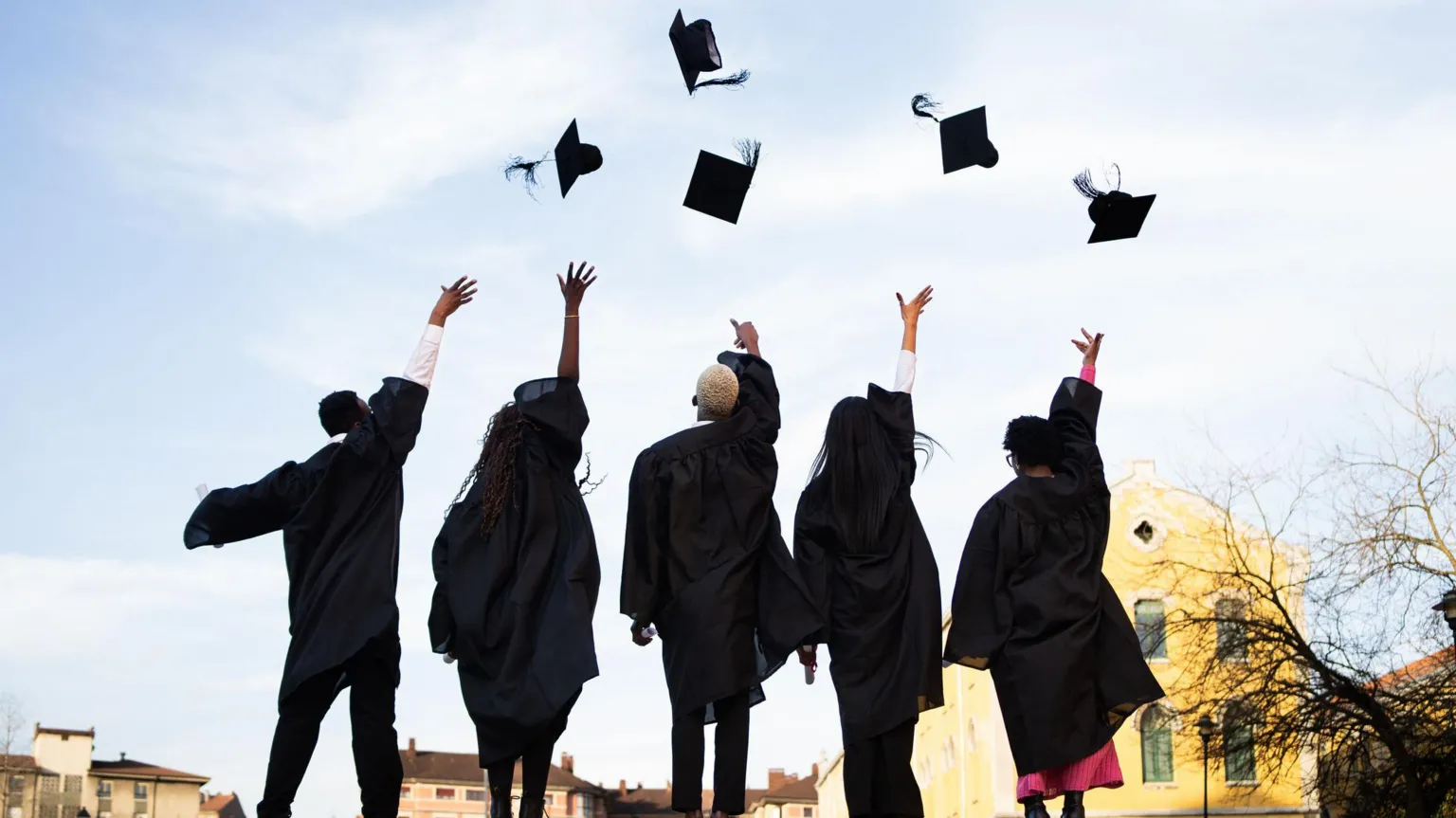  Graduates wearing black robes throwing mortarboards skyward, radiating excitement during commencement ceremony on bright outdoor setting 