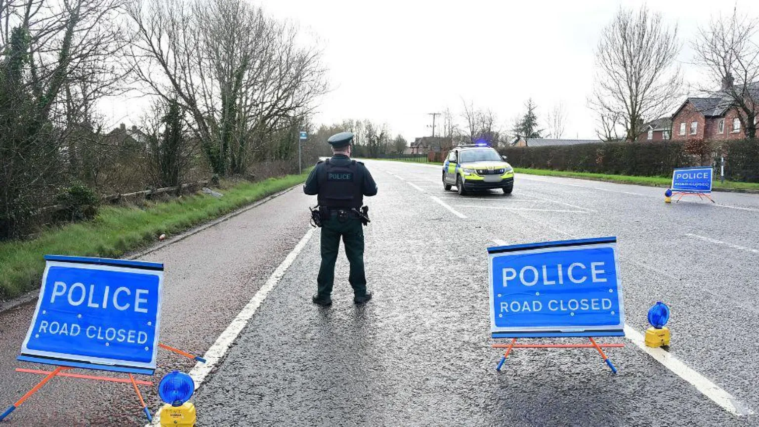 Pacemaker A police officer is standing on a road. His back is turned to the camera. Three signs state police, road closed. A police car is parked on the road. 