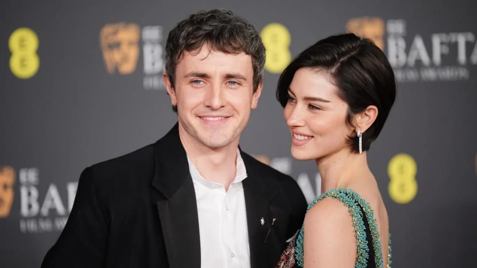  Abrams and Mescal smiling on the red carpet in front of a black background which says Bafta awards on it repeated. Abrams is facing Mescal, and he has an arm around her sitting on her back. They look to the side of the camera. 