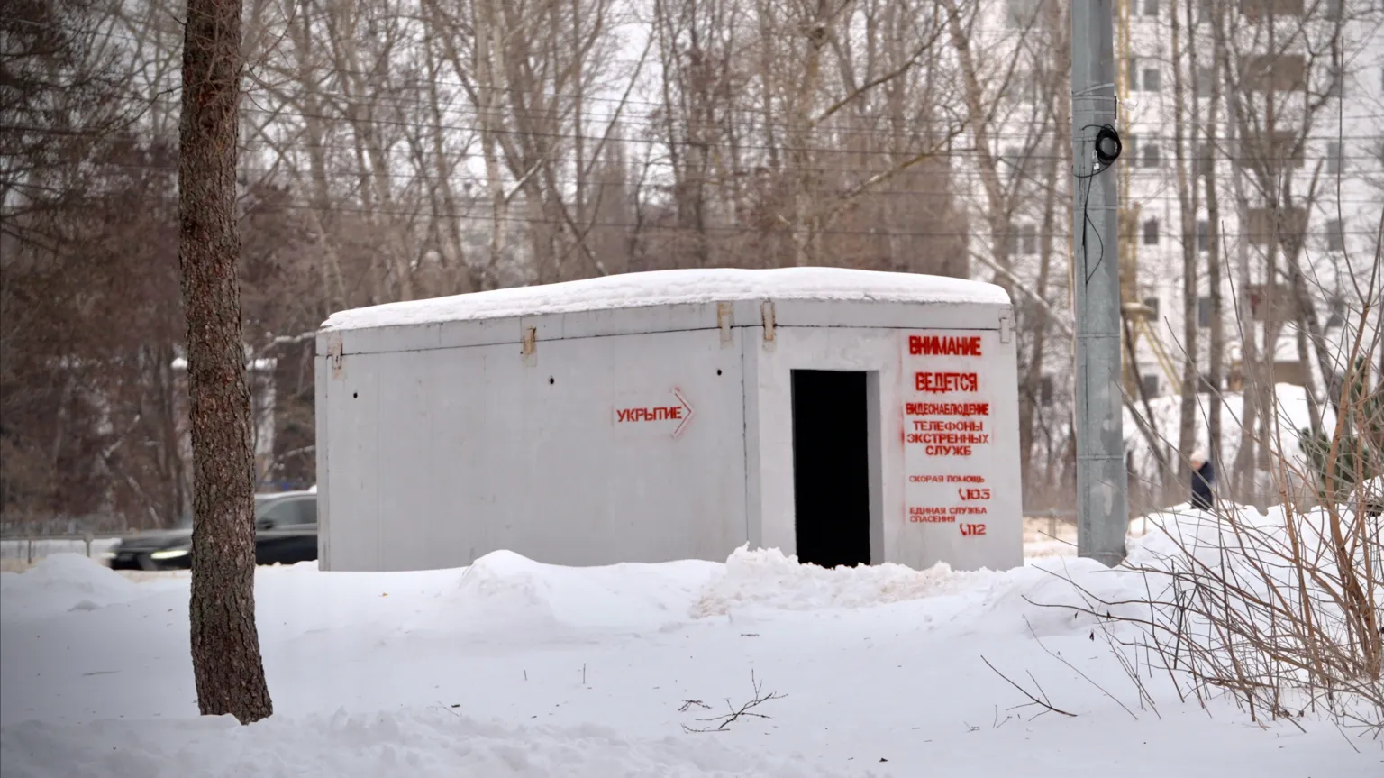 A concrete shelter stands in a snowy park in front of apartment blocks in Yelets