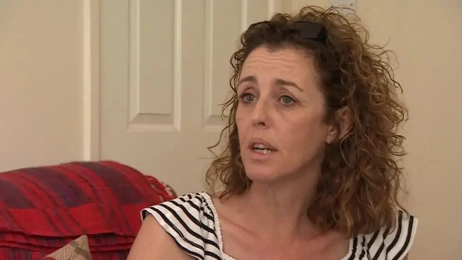 A still image of Nicki Durbin who has shoulder length curly brown hair. She is wearing a black and white striped top.