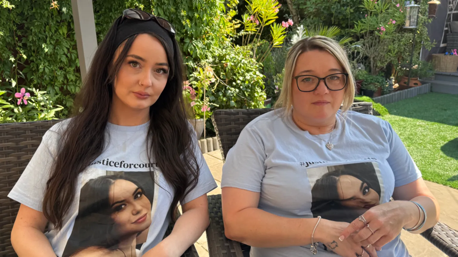 George King/BBC Charleigh and Samantha Mitchell sitting next to each other in two garden chairs in the garden. They are both wearing blue T-shirts with Courtney Mitchell's face on them. They are both looking into the camera.