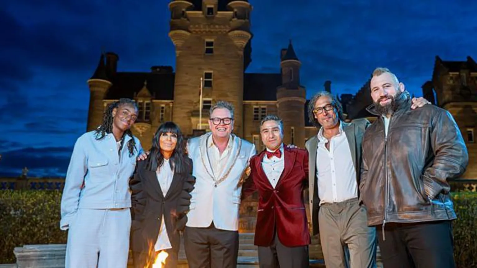 BBC/Studio Lambert/Paul Chappells A group of people, the Celebrity Traitors and Claudia Winkleman, standing in front of a castle with a dark sky behind it.