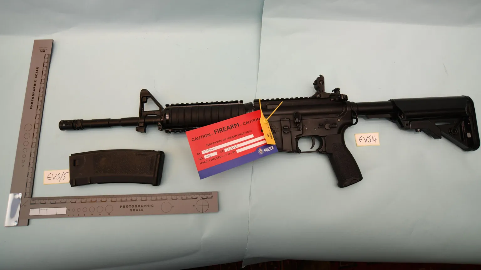 Counter Terror Policing North East A long black air rifle is placed on light blue paper as part of a police evidence photo. There is a red paper label attached that reds: 