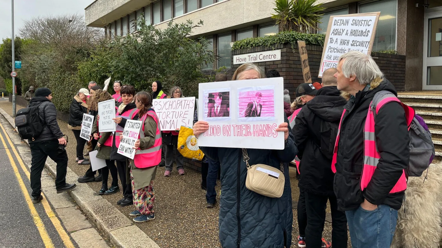 JULIETTE PARKIN/BBC About a dozen people, some wearing purple hi vis waistcoats and some holding up home made placards, stand outside Hove Trial Centre, a grey modern brutalist building.