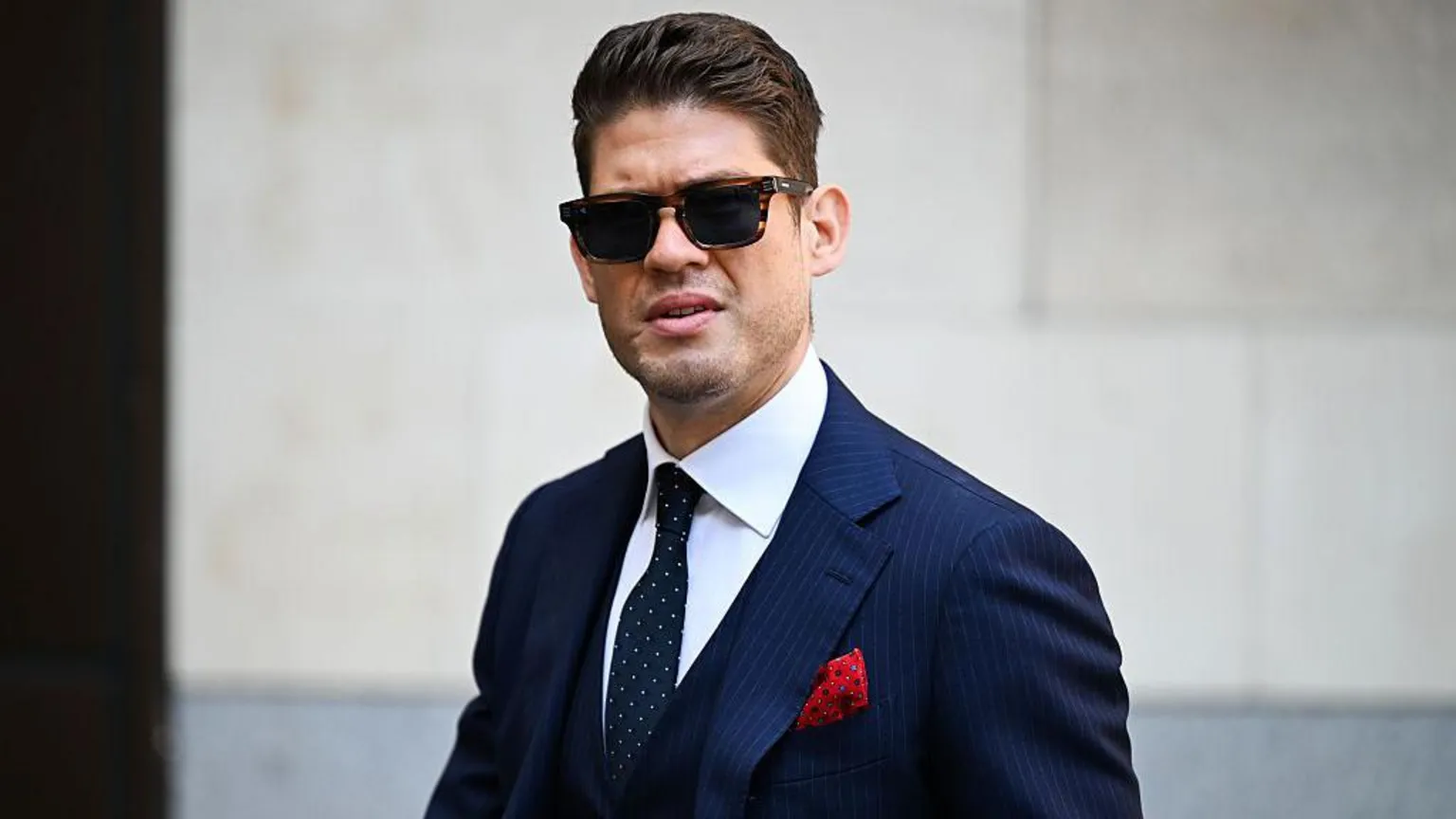 Bloomberg via A man with short brown hair wears dark sunglasses and a blue pinstriped suit with a red pocket square looks without smiling towards the camera.