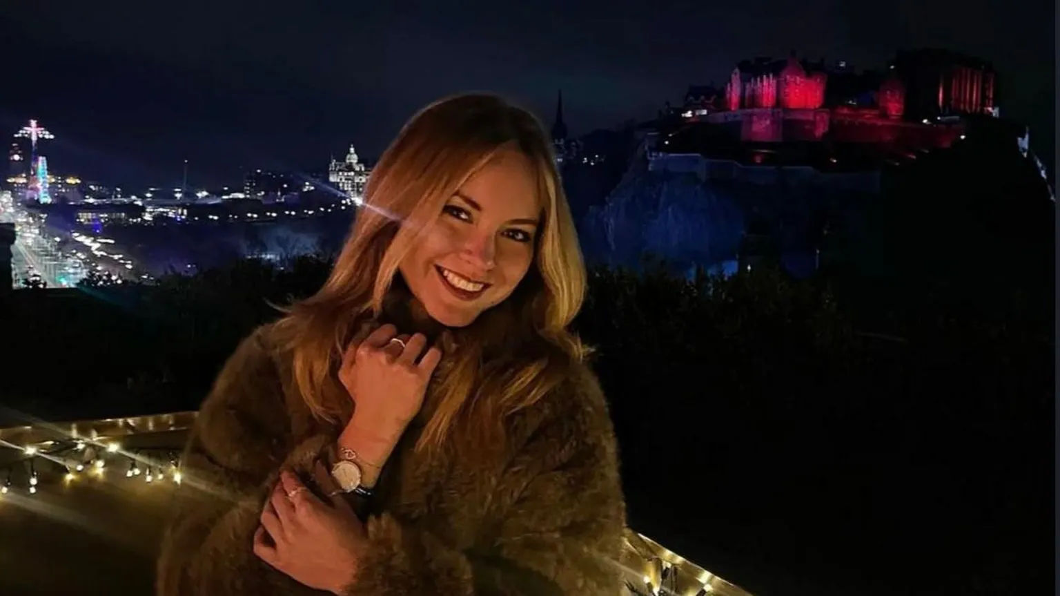 Mira Al Faradz A photo with Anastasiia Korkina on the foreground and Edinburgh castle on the background. The photo is made at night and the Edinburgh castle is lit with pink light.