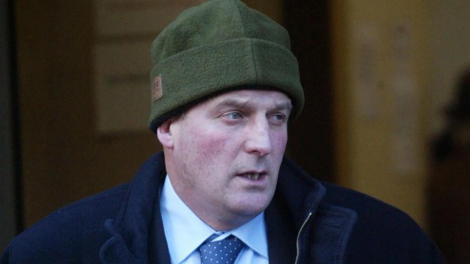  Hector Dick outside court. He is wearing a green beanie hat, a dark blue coat and a light coloured shirt with a blue tie.