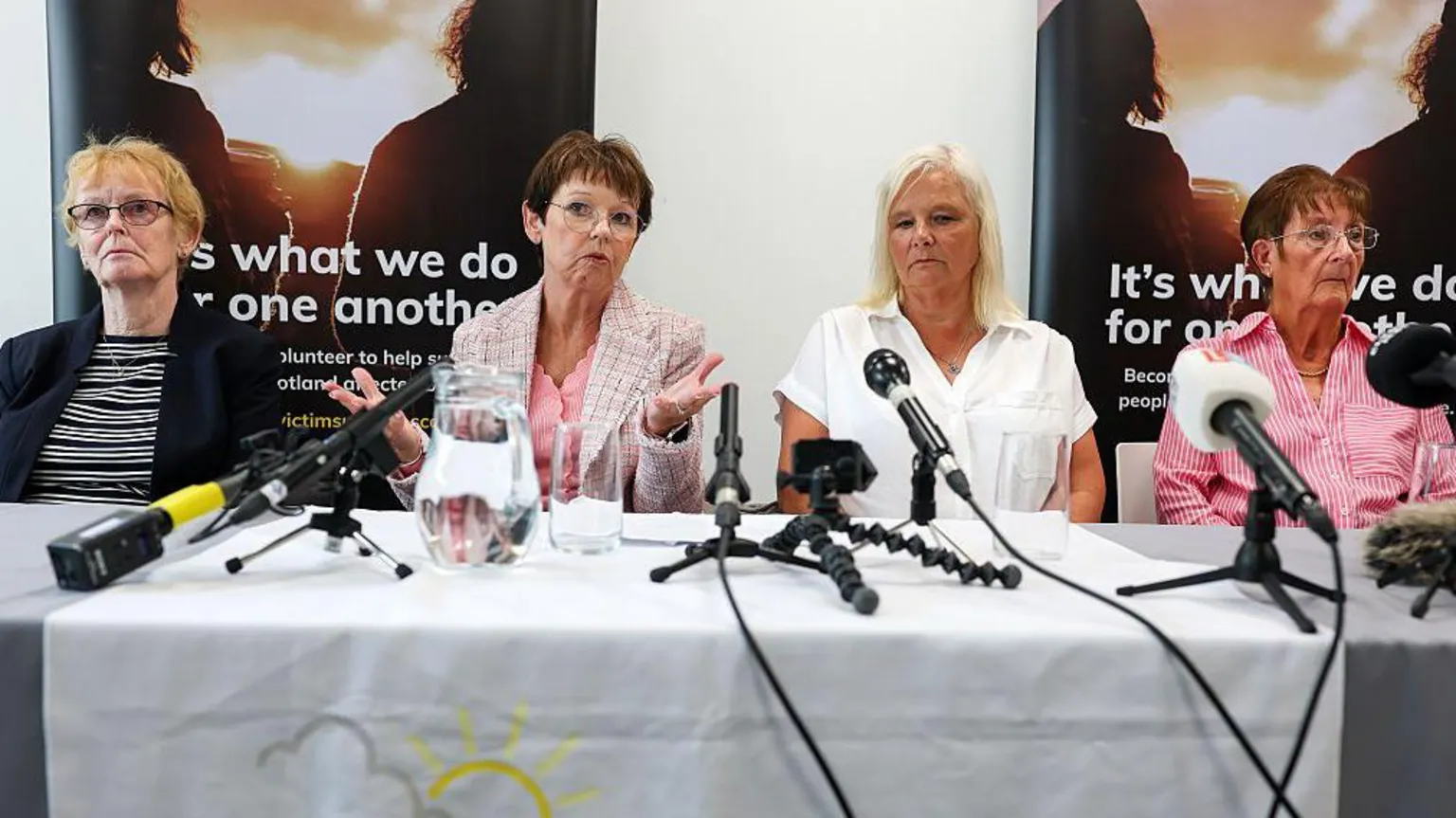  Sitting behind a desk covered with a white fabric are, from left: Arlene's mother Isabelle Thompson and sister Carol Gillies, next to Suzanne Pilley's sister Gail Fairgrieve and mother Sylvia Pilley.