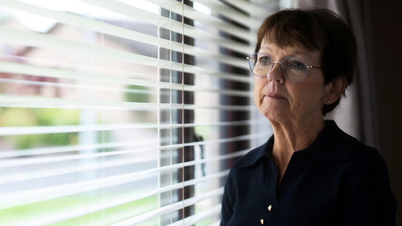 Sean De Francesco/Firecrest Films Carol Gillies looking out of a window. She has short hair and glasses and is wearing a black top.