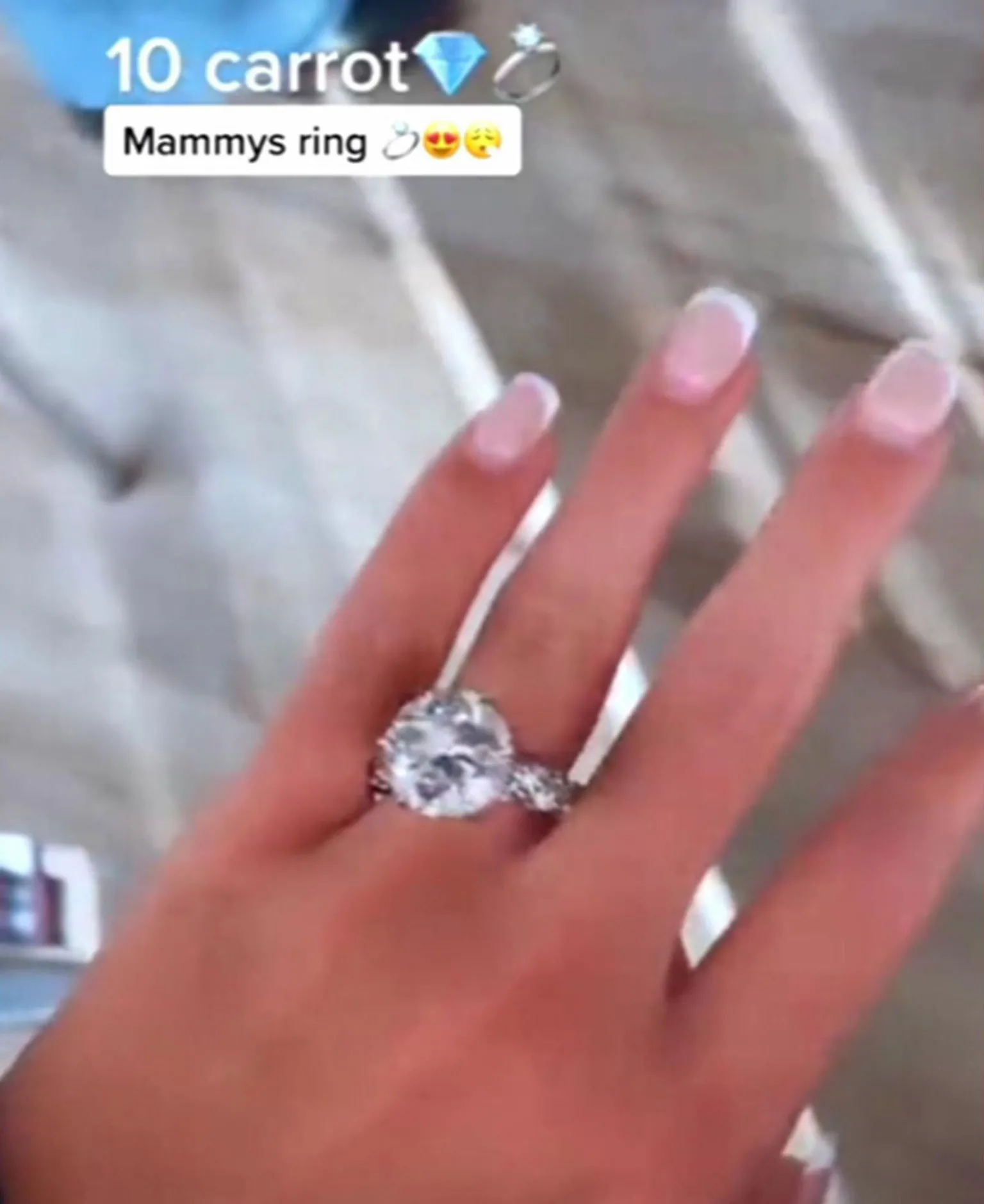 TikTok A large diamond ring set sits on a woman's finger, as she has her hand outstretched. It's set in silver, and has smaller diamonds running down the band of the ring. The background of the image is blurred. Above some text says 