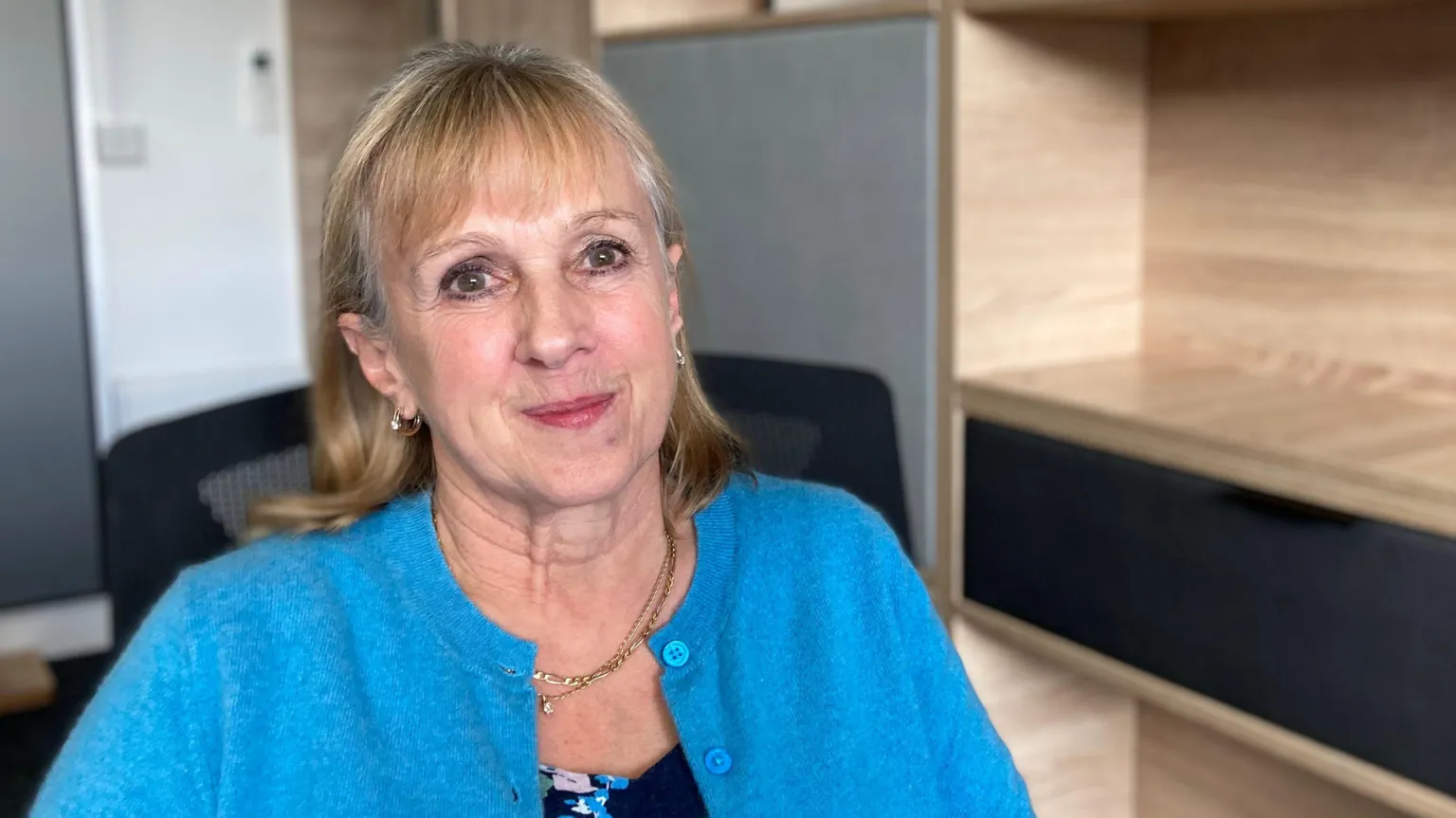 BBC/Simon Spark The managing director of the group of children’s homes, Julie, wears a bright blue, unbuttoned cardigan, over a flowery top. She has shoulder-length, blonde hair, and is sitting in an office chair. 