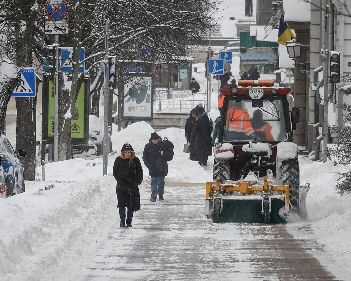 Pedestrians walk next to a snowplough clearing a street after a heavy snowfall on a cold winter day in Kyiv