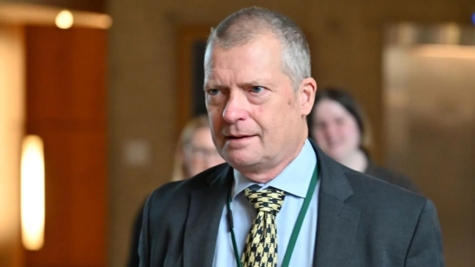  Graham Simpson, who has short grey hair, in a close-up shot. He is wearing a dark suit, light blue shirt and yellow patterned tie. 