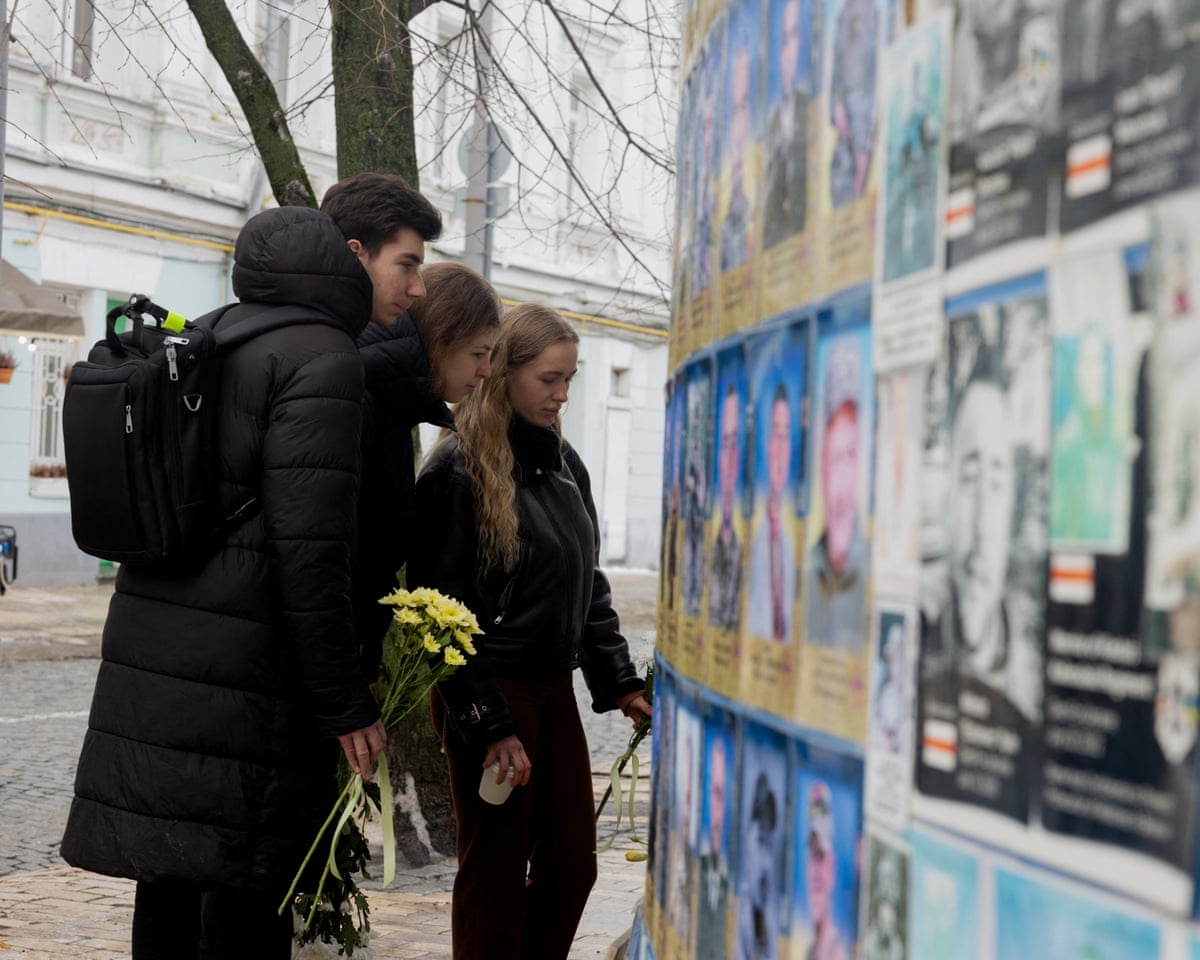 People holding flowers pay their respect as they look at the Wall of Remembrance of the Fallen for Ukraine in Kyiv on February 24, 2026, as Ukraine marks the fourth anniversary of Russia's invasion.