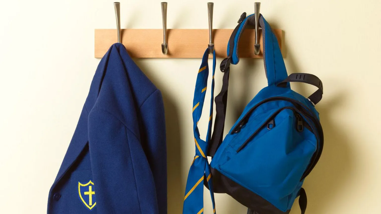  A blue blazer, yellow and blue tie and blue backpack hanging on hooks.