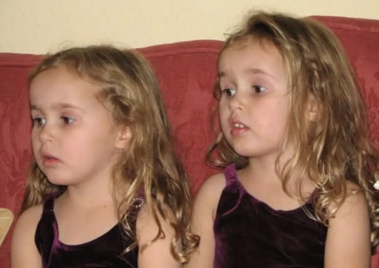 Caitlin and Grace at around four years old. They have blonde hair and both wear purple tops. They look extremely similar.