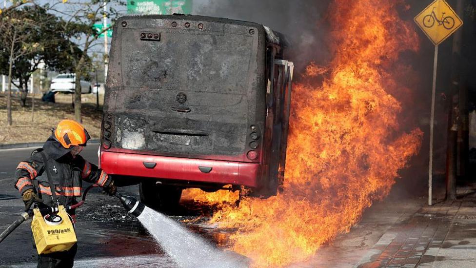 A fireman blasts water against a burning bus in Mexico set alight during a spate of cartel violence