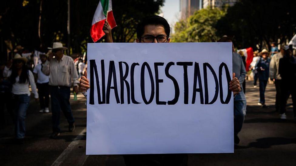 A young male protester holds up a sign reading 'Narcoestado' during an anti-cartel protest in Mexico City, Mexico