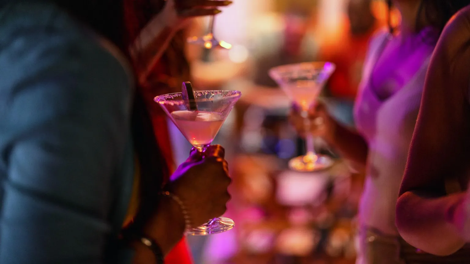  Close-up of a martini glass held by a female at a bar with purple lighting