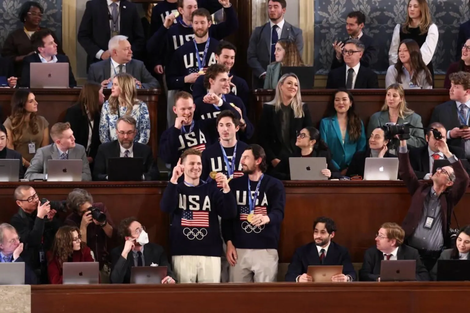  Hockey players hold their god medals while wearing navy sweaters with American flags on them