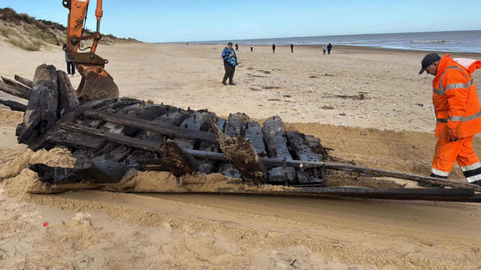 Shaun Whitmore/BBC The timbers from an old boat are moved up the beach. The timbers are leaving a trail in the sand. A man in hi-viz jacket and trousers is walking behind the timbers. In the background, an onlooker is standing on the beach is watching the operation.