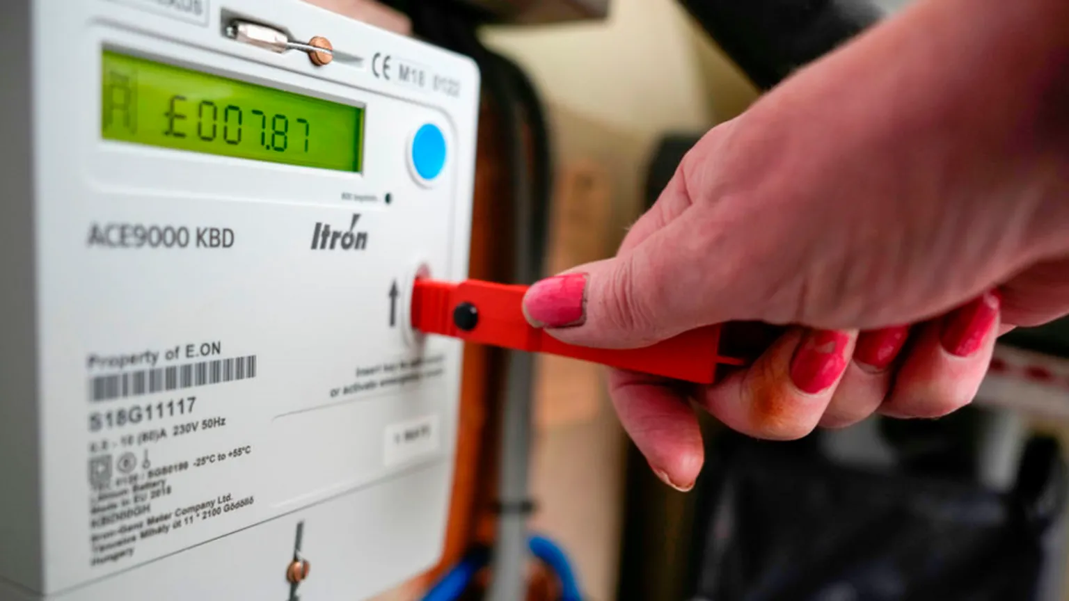  Hand on a key being inserted into a prepayment meter with a display showing £7.87 left in credit.